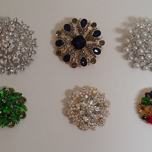 May include: Seven different brooches with various coloured rhinestones and pearls. The brooches are arranged in two rows of three.