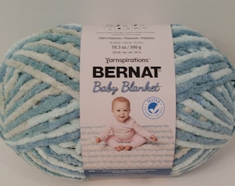 Puede incluir: Una madeja de hilo Bernat Baby Blanket en una combinación de colores azul y blanco. El hilo es 100% poliéster y pesa 300 gramos (10,5 onzas). La etiqueta también dice "Yarnspirations" y "Probado para sustancias nocivas."