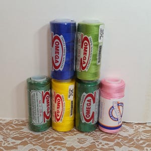 Puede incluir: Seis carretes de hilo de nylon Hilo 100% de la marca Omega, en varios colores: verde, azul, amarillo, verde, rosa. Cada carrete está etiquetado con el nombre de la marca, el tipo de hilo y el tamaño: No. 2 - 275 m.