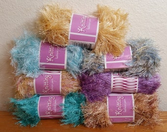 May include: A stack of colorful knitting yarn skeins. The yarn is in various shades, including light blue, gold, purple, and brown. Each skein has a label that reads "Knitting fashion yarn."