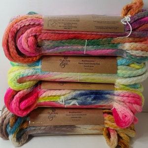 Może przedstawiać: Stos kolorowych, ręcznie farbowanych motków grubej przędzy dziewiarskiej. Przędza ma odcienie różu, żółci, niebieskiego i pomarańczowego. Każdy motek jest oznaczony marką "Yarn Bee" i informacjami o produkcie. Etykiety wskazują na druty do robienia na drutach 10 mm.