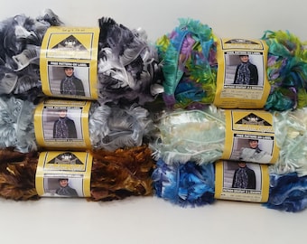 May include: Six skeins of Fashion Light eyelash yarn arranged in two columns. The yarn features a feathery, textured appearance in various colors including grey, brown, blue, green, and cream. Each skein has a yellow label with text.