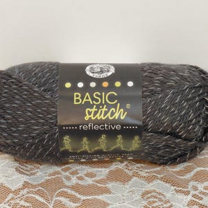 May include: A ball of dark grey Basic Stitch reflective yarn. The yarn has white flecks throughout and a black label with the brand name and running figures. The yarn is anti-pilling acrylic.