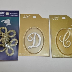 May include: Three packages of gold and white embroidered fabric letters and a gold cord toggle. The letters are on a gold background and the toggle is on a blue background. The packages are labeled "Jar" and "Wrights". The letters are 1 1/2 inches tall.