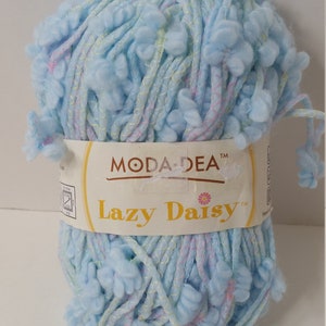 Pode incluir: Um novelo de fio azul claro com detalhes rosa e amarelo. O fio é chamado de "Lazy Daisy" e é uma marca de Moda Dea.