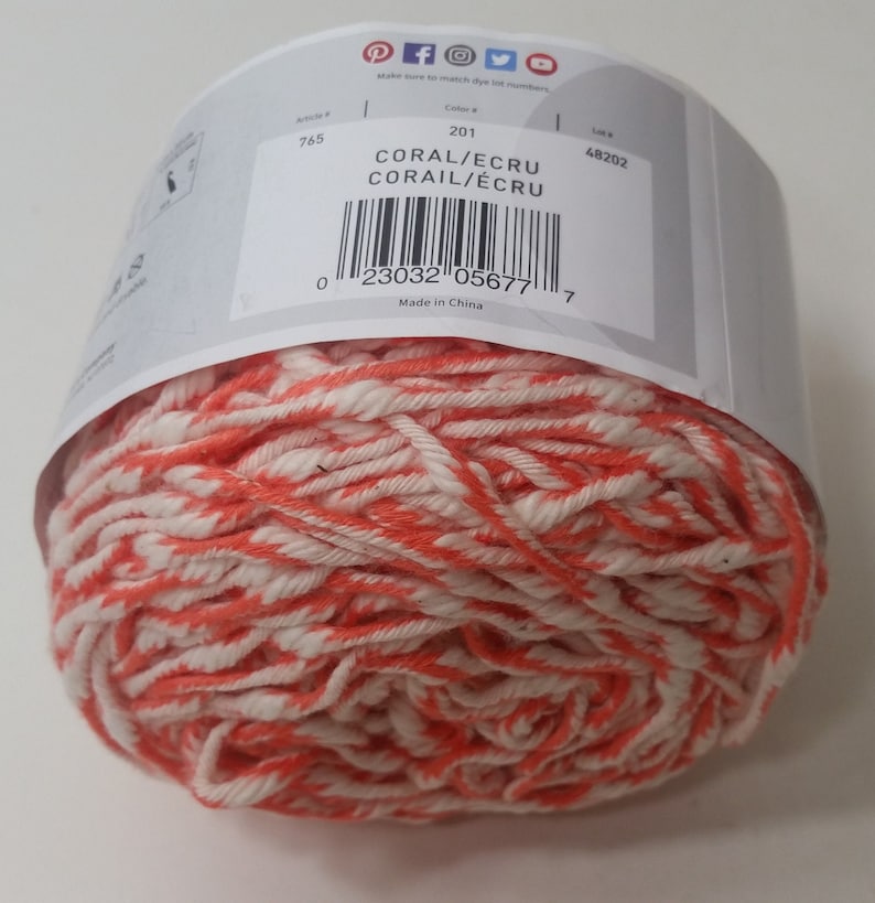 May include: A ball of coral and ecru yarn. The label reads "CORAL/ECRU CORAIL/&Eacute;CRU" and has a barcode. The label also says "Made in China".