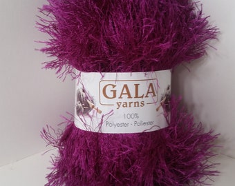 Può includere: Un gomitolo di filato soffice viola scuro con un'etichetta bianca che recita "GALA yarns 100% Polyester - Poliester"