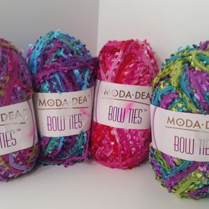 Pode incluir: Quatro novelos de fio Moda Dea Bow Ties em diferentes cores: roxo, turquesa, rosa e verde. Cada novelo tem um rótulo com o nome da marca e a inscrição "Bow Ties".
