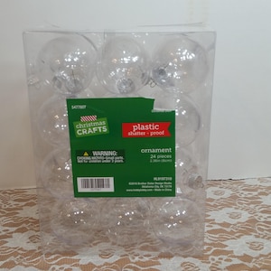 Op de afbeelding: Een verpakking met 24 heldere, onbreekbare kerstballen van plastic. De ballen hebben een diameter van 6 cm. De verpakking is gelabeld met "Christmas Crafts" en "onbreekbare plastic kerstbal".