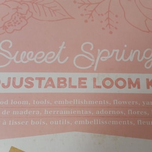 Może przedstawiać: Różowe pudełko z napisem "Sweet Spring" i "ADJUSTABLE LOOM KIT" w kolorze białym. Pudełko zawiera: krosno drewniane, narzędzia, ozdoby, kwiaty i przędzę. Kwiatowe ilustracje w tle.