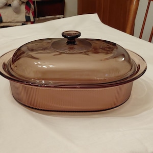 以下が含まれることがあります： 琥珀色のガラス製オーバルキャセロール皿と、それに合う蓋。 皿の側面にはリブ模様があり、蓋には濃い茶色のノブが付いています。 皿は、焼き料理と盛り付け用に設計されています。 長さ約30cm。
