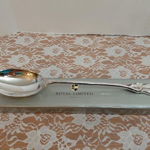 Op de afbeelding: Een zilveren serveerlepel met een grote, ovale kom en een lange, slanke steel. De lepel ligt op een grijze doos met de woorden "ROYAL LIMITED Silver" erop gedrukt. De lepel is ongeveer 30 cm lang.