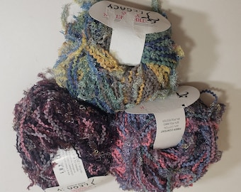 May include: Three skeins of Legacy yarn in various colours. The yarn is a mix of blue, green, yellow, pink, and purple. Each skein has a tag attached. The yarn is made of 50% cotton and 50% polyester.