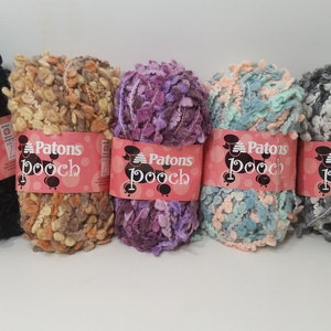 May include: Five balls of Patons Pooch yarn in different colors: black, tan and brown, purple, light blue and pink, and gray and white.