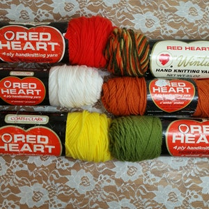 May include: Six skeins of Red Heart brand yarn in various colors, including red, white, yellow, green, orange, and a multi-colored skein. The yarn is labeled as 4-ply handknitting yarn.