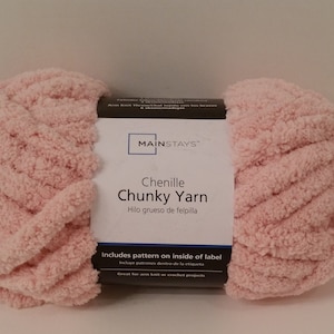 Könnte beinhalten: Ein rosa Knäuel Mainstays Chenille Chunky Garn. Das Etikett lautet "Chenille Chunky Yarn" und "Hilo grueso de felpilla". Außerdem steht darauf "Includes pattern on inside of label" und "Great for arm knit or crochet projects".