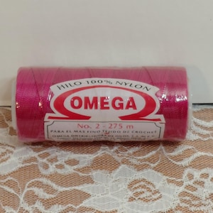 May include: A spool of bright pink Omega crochet thread. The label reads "HILO 100% NYLON OMEGA No. 2 - 275 m PARA EL MAS FINO TEJIDO DE CROCHET". The thread is wrapped in clear plastic.