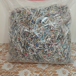 May include: A clear plastic resealable bag filled with a large quantity of multicolored shredded paper strips. The shredded material consists of various thin, narrow pieces of paper in assorted colors, including white, blue, red, and black.