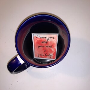 Peut inclure: Une tasse en c&eacute;ramique bleue avec une bande blanche sur la poign&eacute;e. &Agrave; l'int&eacute;rieur de la tasse se trouve une carte blanche avec un fond aquarelle rouge et le texte "I crave your soul, your mind & your body".