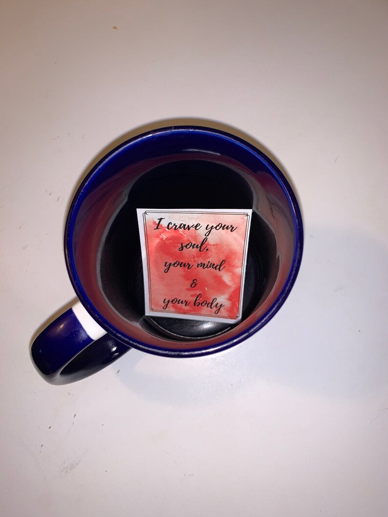 Peut inclure: Une tasse en c&eacute;ramique bleue avec une bande blanche sur la poign&eacute;e. &Agrave; l'int&eacute;rieur de la tasse se trouve une carte blanche avec un fond aquarelle rouge et le texte "I crave your soul, your mind & your body".