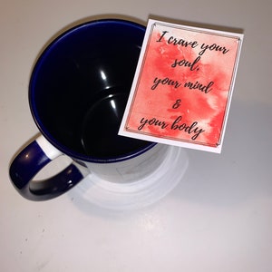 Peut inclure: Une tasse en c&eacute;ramique bleue avec un bord et une poign&eacute;e blancs. Une carte aquarelle rouge avec le texte "I crave your soul, your mind & your body" est plac&eacute;e sur la tasse.