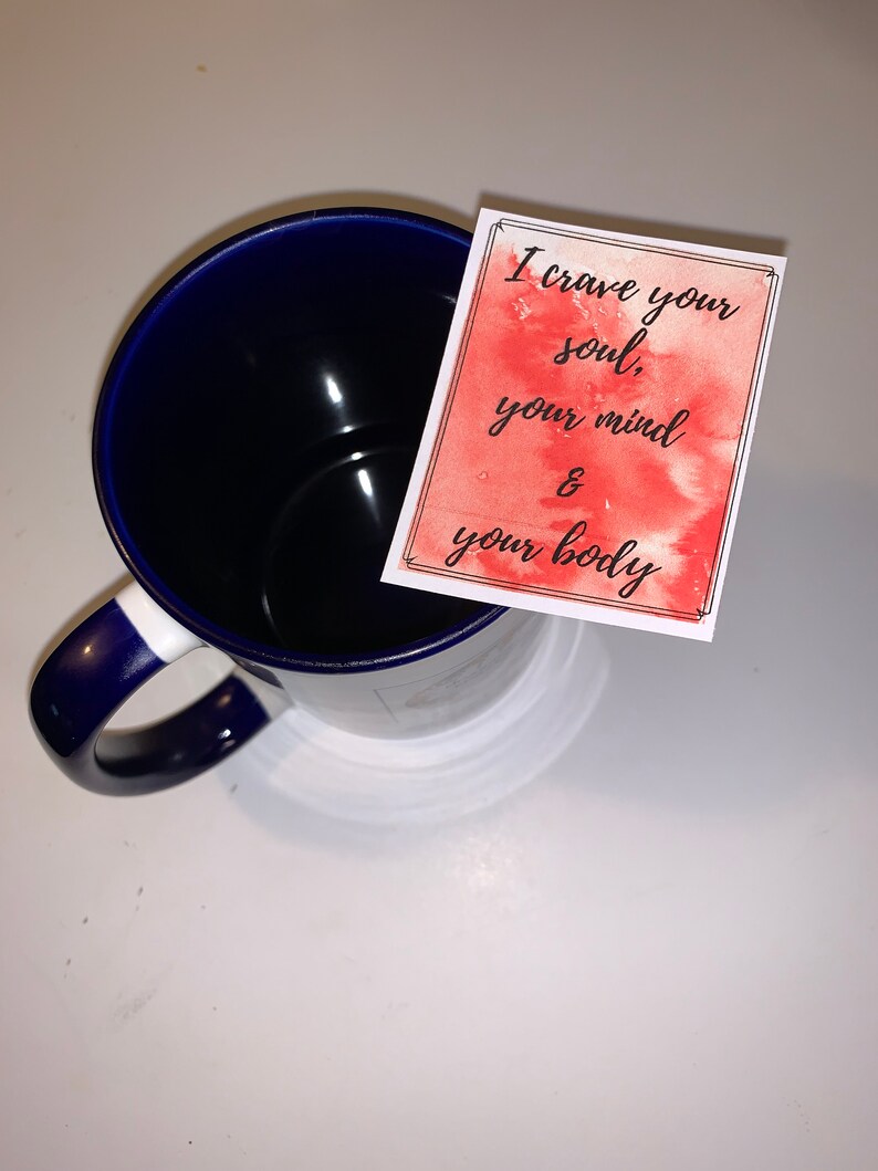 Peut inclure: Une tasse en c&eacute;ramique bleue avec un bord et une poign&eacute;e blancs. Une carte aquarelle rouge avec le texte "I crave your soul, your mind & your body" est plac&eacute;e sur la tasse.