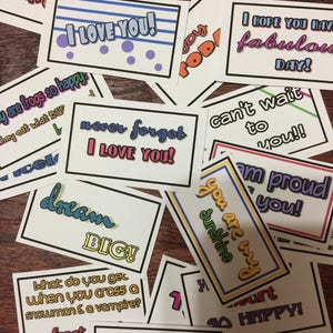 Może przedstawiać: Zbiór kolorowych kartek z różnymi wiadomościami i żartami. Kartki są wydrukowane na białym papierze z czarnymi obramowaniami i mają żywe kolory, takie jak czerwony, niebieski, żółty i zielony. Niektóre z wiadomości to "Kocham cię", "Marz o wielkim", i "Jesteś moim słońcem".