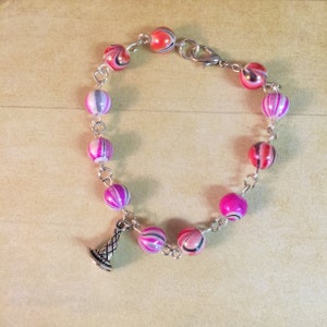 May include: A pink and red striped beaded bracelet with a silver charm in the shape of a cone.