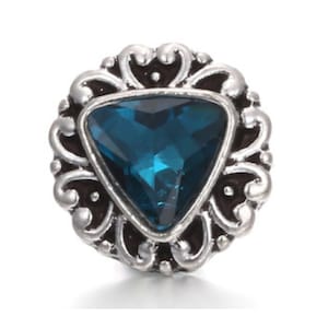 Puede incluir: Un charm plateado con un brillante triangular azul en un marco de filigrana decorativo.