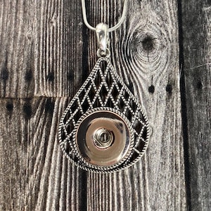 以下が含まれることがあります： 装飾的な幾何学模様が施された、銀色の涙滴型のペンダント。ペンダントの中央には、丸い銀色のボタンが付いています。