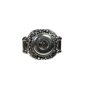 May include: Silver ring with a decorative, ornate design. The ring features a round, silver button in the center.