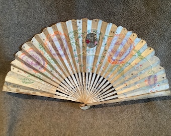 May include: A vintage hand fan with a white, blue, and gold background. The fan is decorated with painted flowers and leaves in shades of pink, purple, and orange.