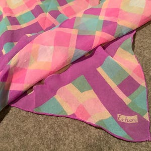 Può includere: Una sciarpa a quadri rosa e viola con un bordo a festoni e la parola "Echo" stampata nell'angolo in basso a destra.