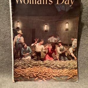 May include: A vintage cover of Woman's Day magazine from October 1946. The cover features a group of people harvesting corn in a barn. The cover is illustrated in a realistic style with warm colors.