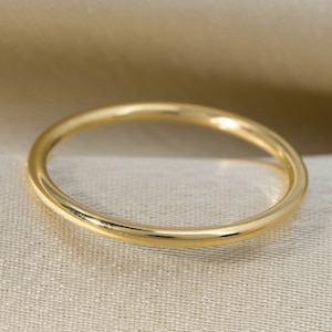 Może przedstawiać: Prosty złoty pierścionek, pokazany na kremowym tle z tkaniny.