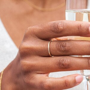 Może przedstawiać: Osoba w białej koszulce bez rękaw&oacute;w i złotym naszyjniku trzyma kieliszek szampana. Osoba nosi złoty pierścionek na palcu.