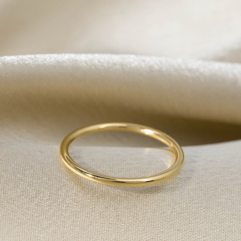 Może przedstawiać: Prosty złoty pierścionek, pokazany na kremowym tle z tkaniny.
