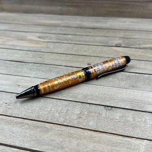 May include: A gold and black pen with a circuit board design. The pen is lying on a wooden surface.