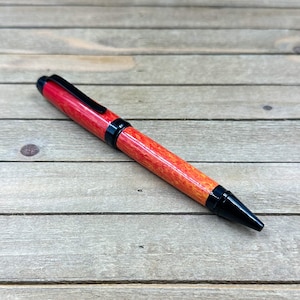 May include: A handcrafted pen with a vibrant red and yellow wood grain pattern. The pen features black accents on the clip, tip, and center band. The pen is a writing instrument.