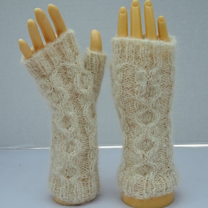 May include: A pair of cream-colored fingerless gloves made of a soft, fuzzy yarn. The gloves have a cable knit pattern and are displayed on a pair of hands.