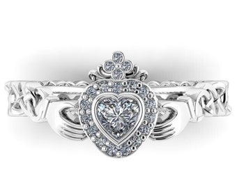 Puede incluir: Un anillo de nudo celta de plata con una piedra central en forma de corazón y una parte superior en forma de corona. El anillo está engastado con pequeños diamantes.