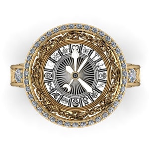 Puede incluir: Un anillo de oro con un diseño circular que presenta una esfera blanca con marcas negras y una aguja dorada. El anillo está engastado con pequeños diamantes alrededor del borde.