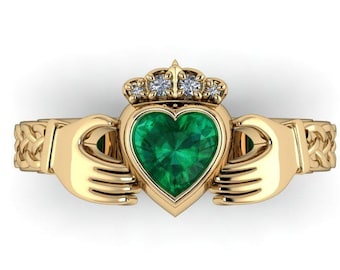 May include: A gold Celtic Claddagh ring with a green heart-shaped emerald gemstone and a crown of small diamonds.