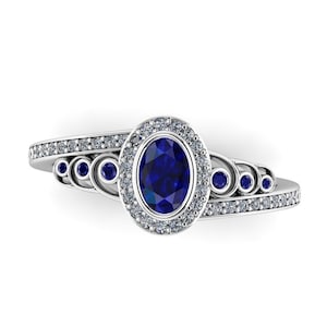 May include: A silver ring with a blue oval sapphire surrounded by a halo of smaller diamonds. The band is adorned with smaller blue sapphires.
