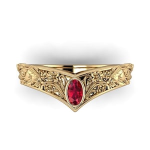 May include: A gold-colored ring with an oval, red gemstone at the center. The ring features intricate floral and leaf patterns along the band. The design is symmetrical, with the gemstone set in a V-shaped setting.