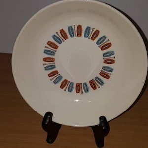 Puede incluir: Un tazón de cerámica blanco con un patrón geométrico en tonos azules, naranja y marrón. El patrón es un círculo de formas repetidas alrededor del centro del tazón.