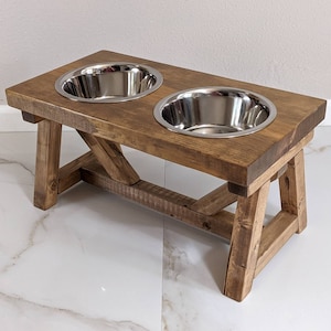 May include: A rustic wooden dog bowl stand with two stainless steel bowls. The stand has a dark brown stain and is made of reclaimed wood.