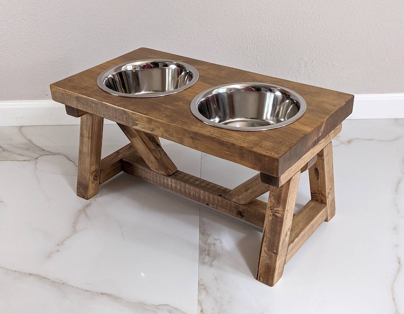 May include: A rustic wooden dog bowl stand with two stainless steel bowls. The stand has a dark brown stain and is made of reclaimed wood.