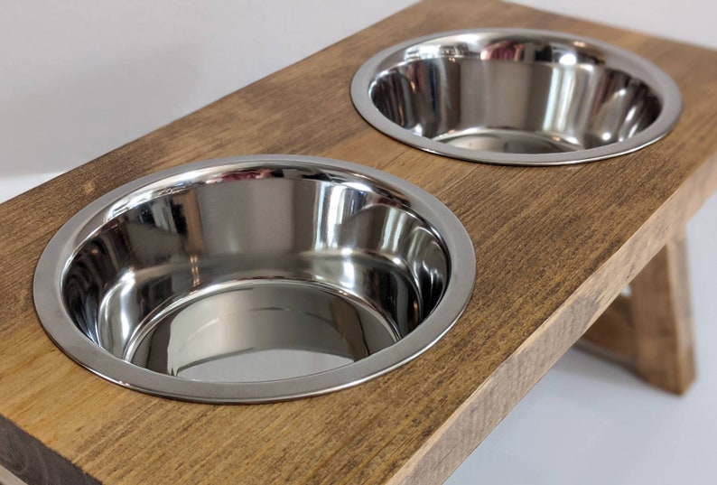May include: A wooden elevated dog bowl stand with two stainless steel bowls. The stand is stained a dark brown color.