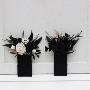 May include: Two black ribbon bookmarks with floral embellishments. One bookmark features white flowers and gold accents, while the other features black flowers.